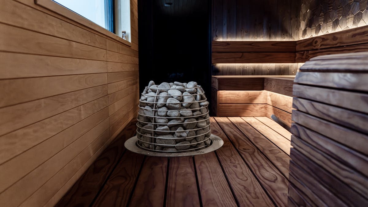 Contemporary indoor sauna with wood panels and stone electric heater, ideal for relaxation.